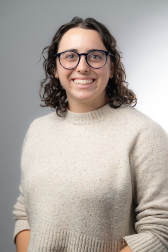 Headshot of doctoral student Rebekah Stein wearing a cream colored sweater, smiling at the camera, against a gradient gray background.