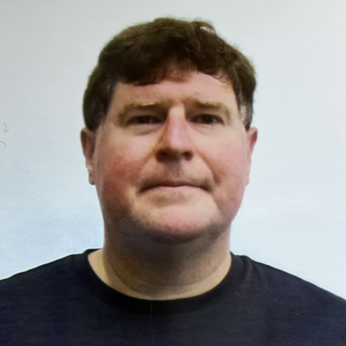 Headshot of faculty member Andrew Wilcock smiling subtly at the camera, wearing a black shirt with a solid light gray background.
