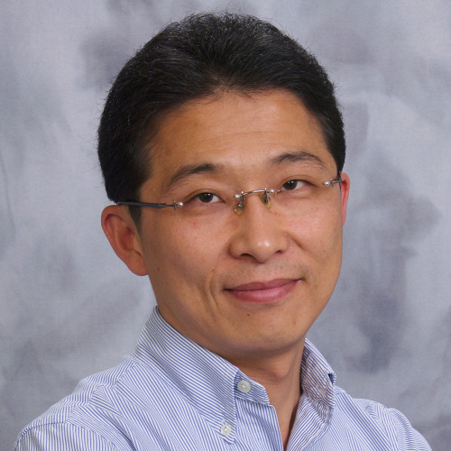 Headshot of faculty member Daeho Kim smiling at the camera in a button down shirt, wearing glasses, with a light blue-gray gradient background