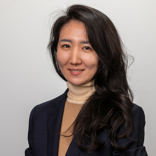 Headshot of doctoral student Minji Kim wearing a dark blazer and turtleneck, smiling at the camera against a light gray backdrop.