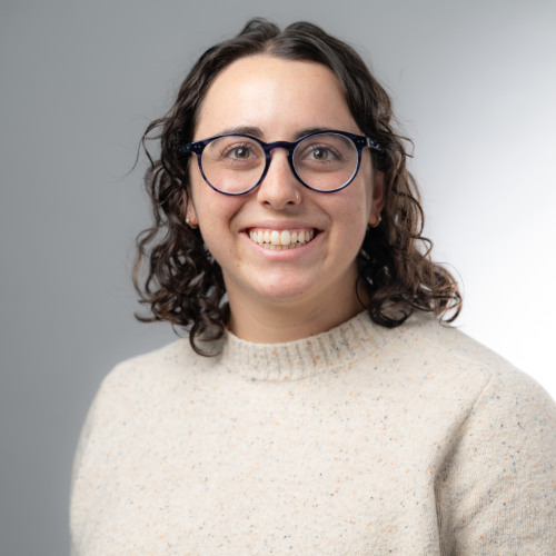 Headshot of doctoral student Rebekah Stein wearing a cream colored sweater, smiling at the camera, against a gradient gray background.